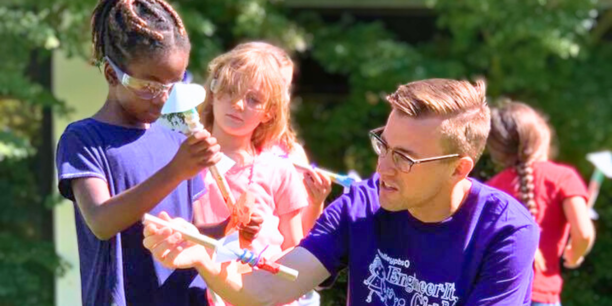 Group of children engaged in STEM learning with camp counselor, participating in collaborative science and technology activities