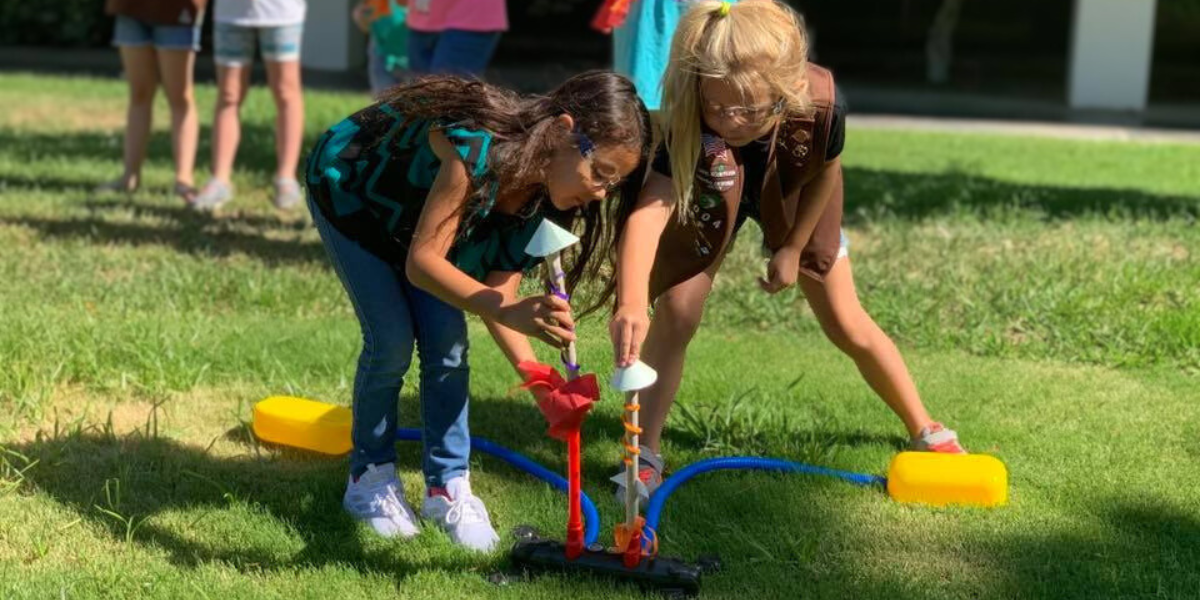 Two children in a STEM summer camp communicating and coordinating to successfully launch a rocket, showcasing teamwork and problem-solving skills.