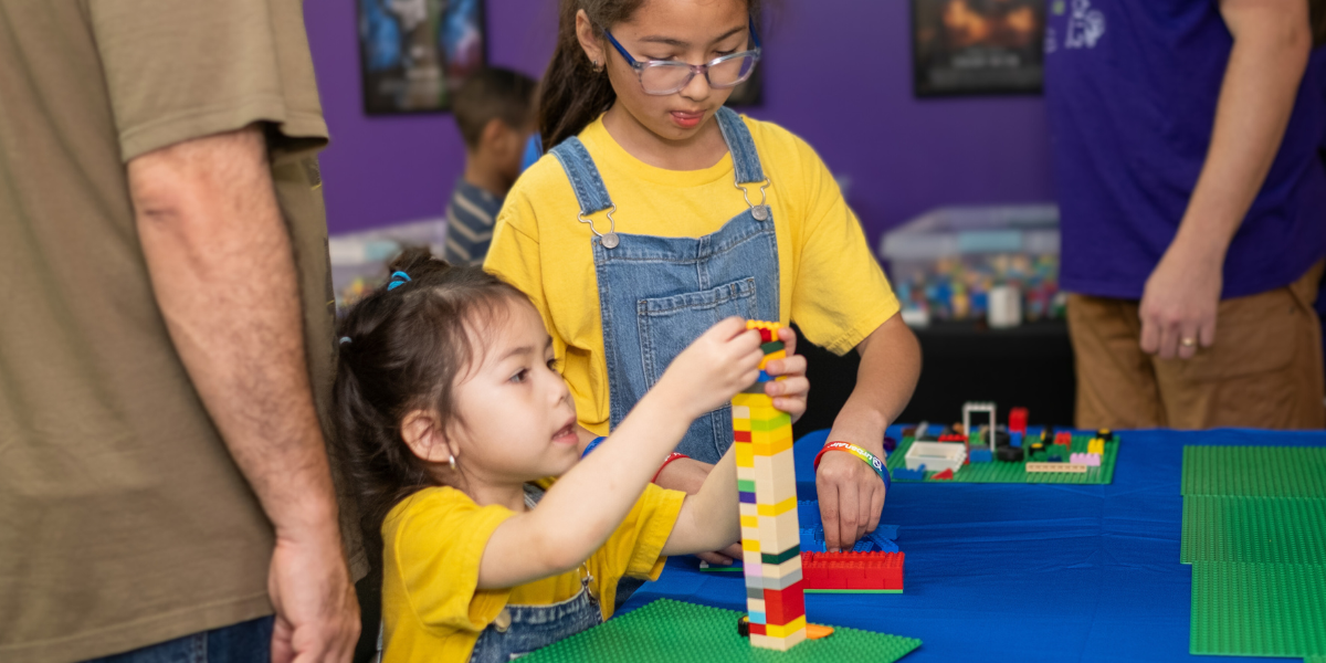 Two children working together to engineer a Lego tower, demonstrating collaboration and hands-on learning in a fun, educational setting.