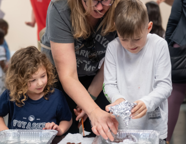 A group of children brainstorming and experimenting with a mentor to address a water displacement challenge, encouraging creativity and innovation.