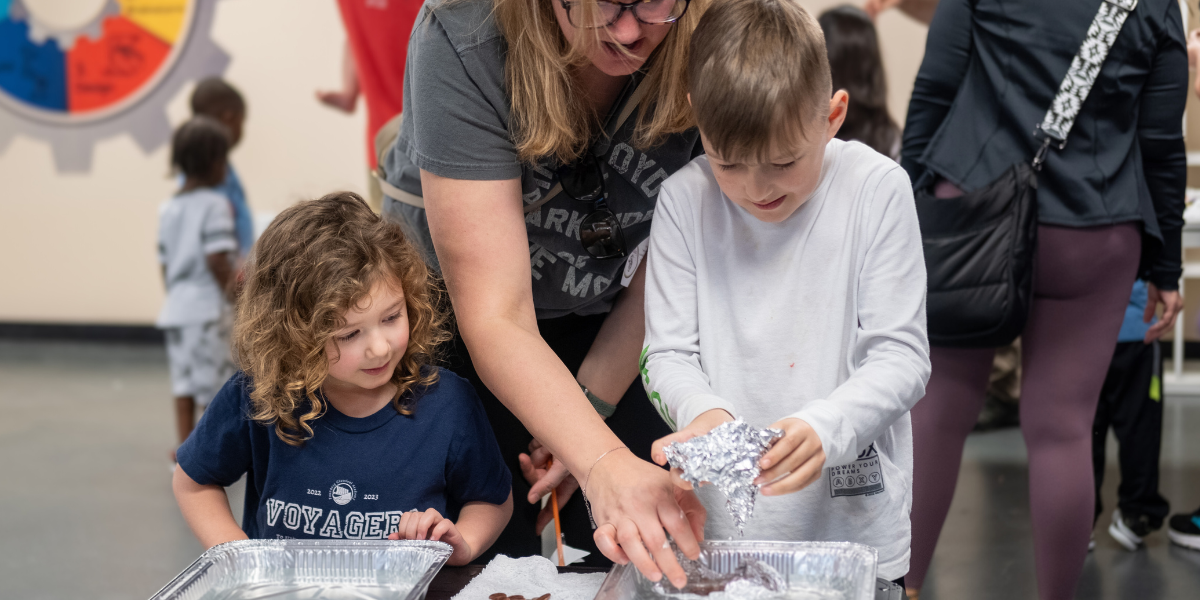 A group of children brainstorming and experimenting with a mentor to address a water displacement challenge, encouraging creativity and innovation.